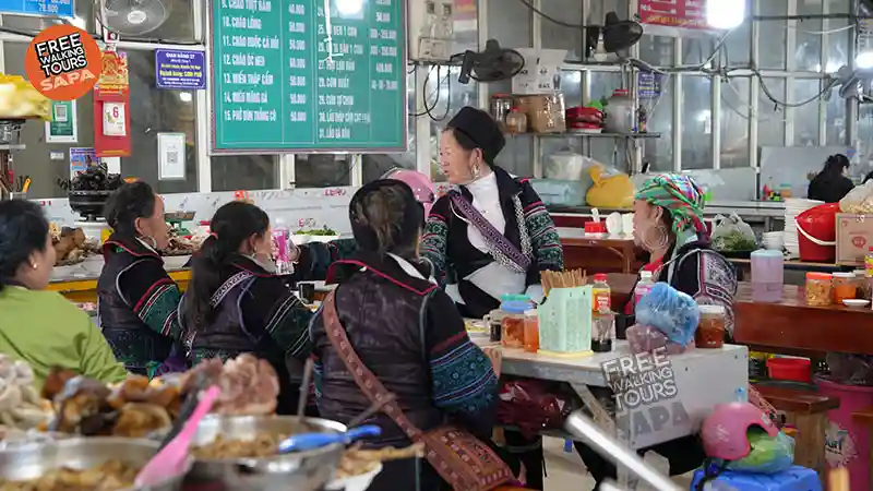 Hmong women in traditional indigo dress sharing a hot meal at a local food court inside Sapa Market in northern Vietnam