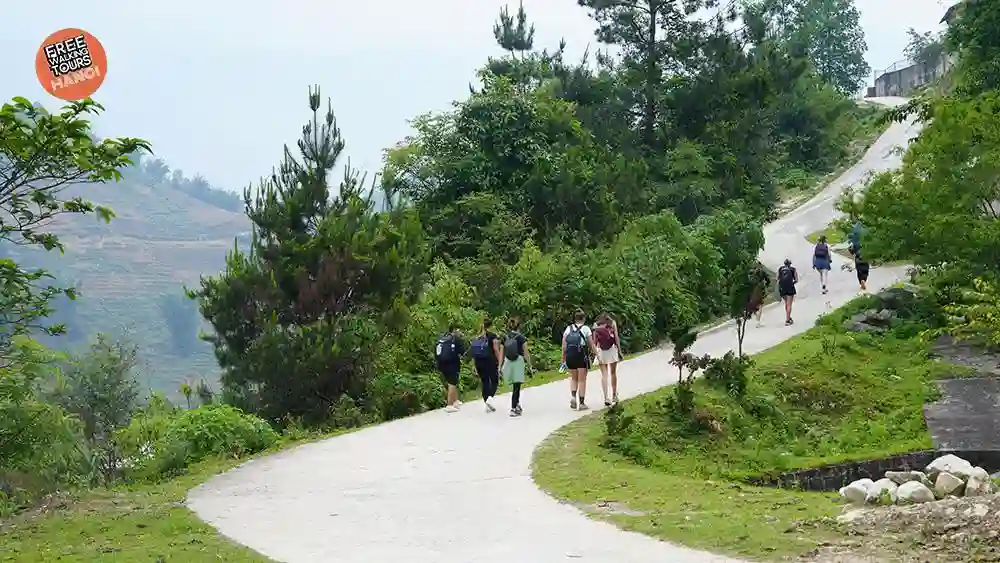 Small group of travelers walking along a quiet hillside path on a Free Walking Tours Sapa trek, with green Muong Hoa Valley terraces in the background