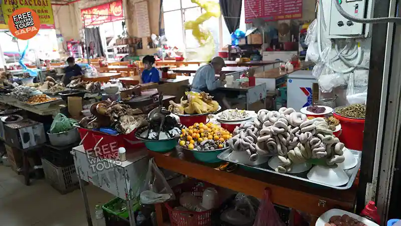 Sapa Food Market stalls displaying smoked buffalo meat, free-range chicken, mountain herbs and seasonal produce inside the local three-story market hall